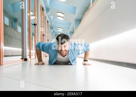 Smiling businessman doing push ups in office corridor Stock Photo