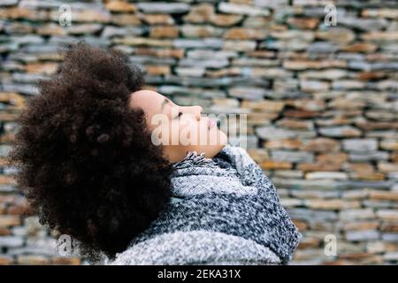 Young woman with eyes closed in warm clothing by stone wall Stock Photo