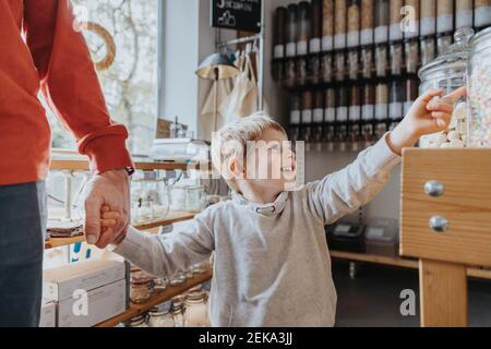 Cheerful boy holding hand of father while pointing at candy jar in store Stock Photo