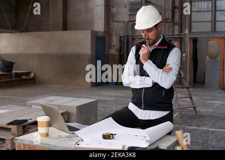 Male architect thinking while analyzing blueprint on table in building Stock Photo