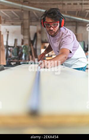 Concentrated male carpenter measuring length using tape measure in workshop Stock Photo