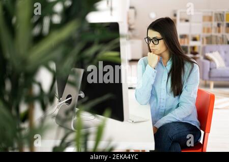 Thoughtful businesswoman with hand on chin looking away while sitting at office Stock Photo