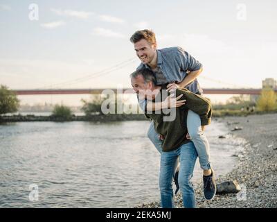 Happy father giving piggyback ride to son at riverbank Stock Photo