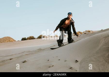 Young man looking away while sandboarding against clear sky at Almeria, Tabernas desert, Spain Stock Photo