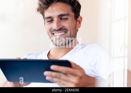Mid adult man smiling while using digital tablet at home Stock Photo