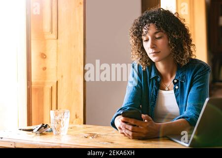 Young female freelancer using smart phone at home office Stock Photo