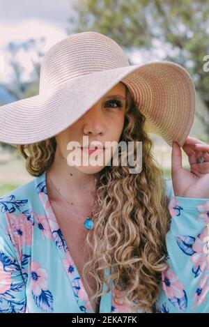 Young woman covering eye with sun hat in park Stock Photo