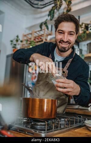 Smiling male chef putting seasoning while cooking food in kitchen Stock Photo