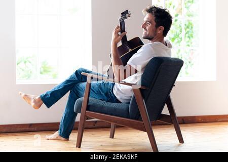 Mid adult man smiling while playing guitar at home Stock Photo