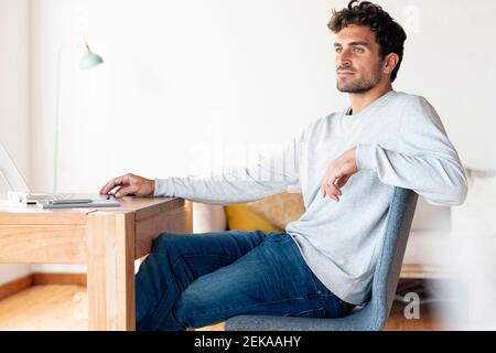 Man looking away while sitting by table at home office Stock Photo