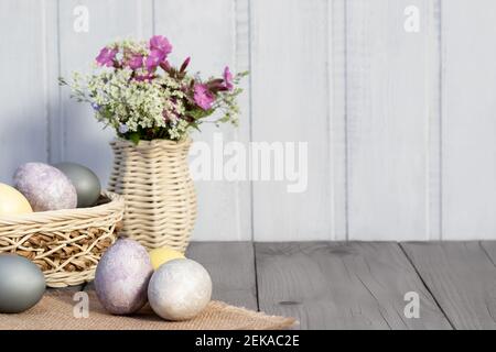 Easter composition - several eggs painted with natural dyes and wildflowers in a vase. Stock Photo