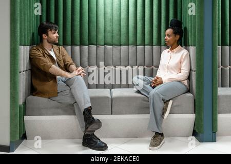 Creative male and female colleagues discussing while sitting on sofa at work place Stock Photo