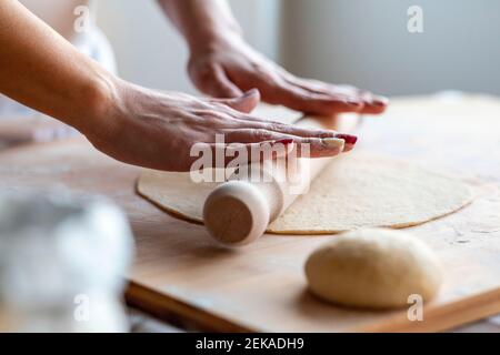 Woman rolling dough on cutting board with rolling pin to make croissants in kitchen Stock Photo