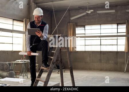 Smiling male building contractor using digital tablet while standing inside site Stock Photo