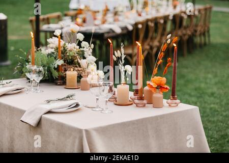 Candles, dried flowers and accessories, bouquets and glasses on table with linen tablecloth on newlywed table Stock Photo