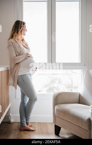 Pregnant woman with hands on stomach standing by window Stock Photo