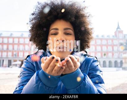 Afro woman blowing confetti while standing in city Stock Photo