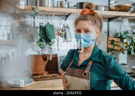 Confident chef wearing protective face mask staring while standing in kitchen during COVID-19 Stock Photo