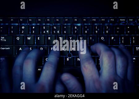 hands typing on keyboard in blue light with motion blur Stock Photo