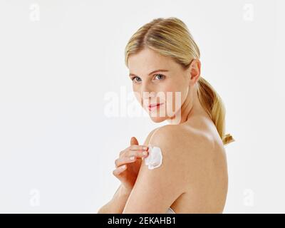 Young woman applying cream on hand while standing against white background Stock Photo