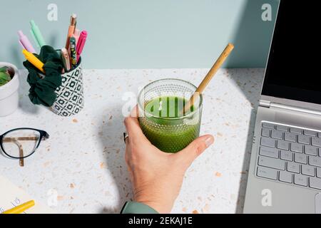 Woman's hand holding healthy green juice on desk at home Stock Photo