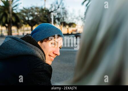 Smiling young man wearing knit hat with girlfriend at promenade Stock Photo