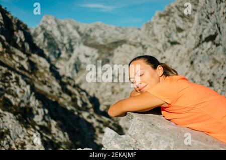 Woman with eyes closed relaxing on rock at Cares Trail in Picos De Europe National Park, Asturias, Spain Stock Photo