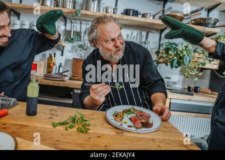 Happy chef looking at colleagues distracting him while working in kitchen Stock Photo