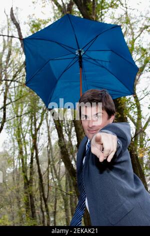 Businessman holding an umbrella and pointing towards camera Stock Photo