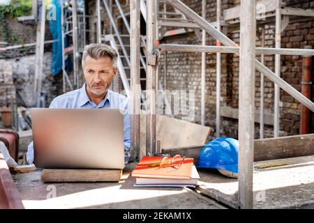 Mature engineer working on laptop while sitting at construction site Stock Photo