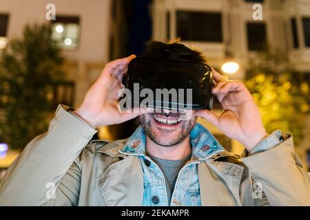 Mid adult man wearing virtual reality headset while sitting outdoors Stock Photo