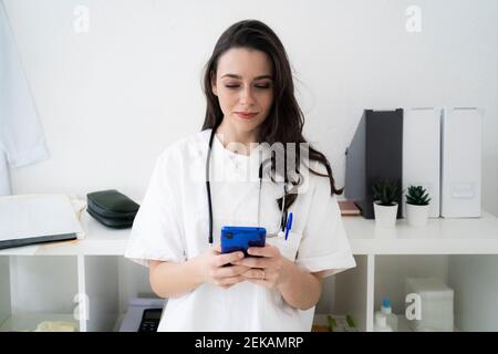 Female doctor text messaging on smart phone in clinic Stock Photo