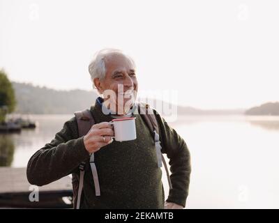 Smiling man with backpack drinking coffee while standing against sky Stock Photo
