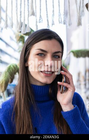 Smiling woman with gray eyes talking on mobile phone against plant Stock Photo