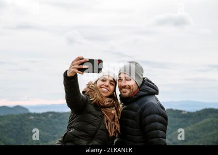 Smiling tourist couple taking selfie against sky during winter Stock Photo