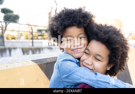 Smiling sibling embracing each other while standing at park Stock Photo