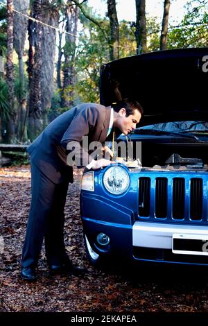 Businessman looking under hood of a car Stock Photo