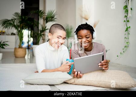 Happy female colleagues using digital tablet while lying on front in living room Stock Photo