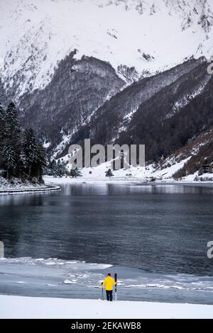 Young man with ski at snow covered lakeshore in front of mountains Stock Photo