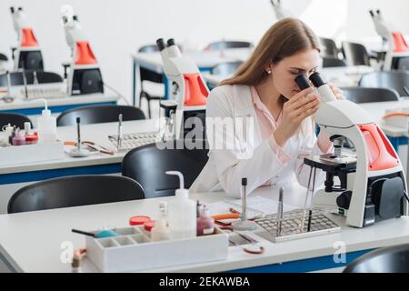 Young researcher in white coat working with microscope in lab Stock Photo