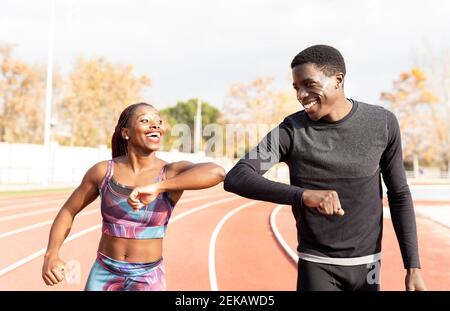 Male and female athlete doing elbow bump while walking on track during sunny day Stock Photo