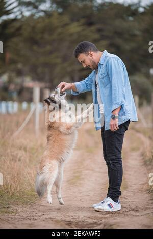 Man feeding dog while standing on dirt road Stock Photo