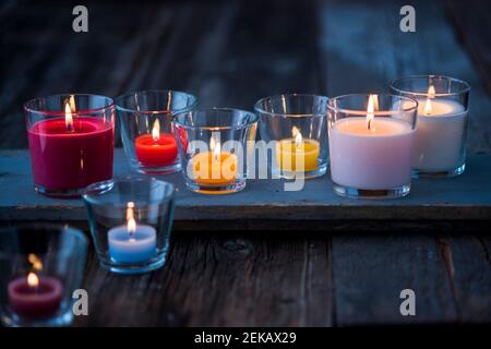 Colorful glass candles burning on wooden surface Stock Photo