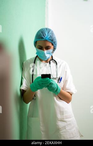 Female doctor using smart phone while leaning by wall at clinic Stock Photo