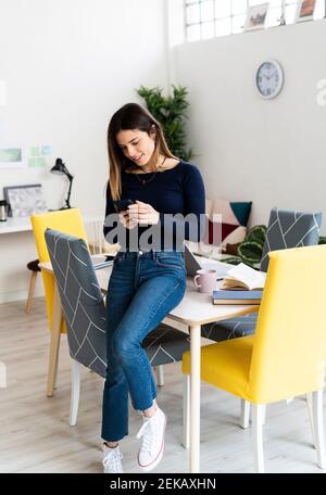 Young female student studying on smart phone while sitting on table at home Stock Photo