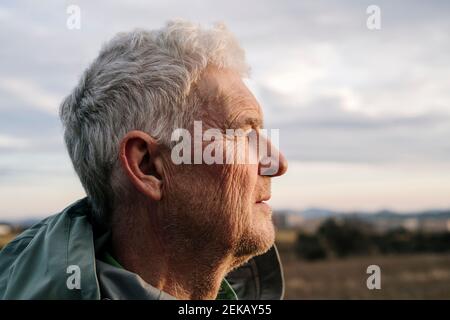 Senior man with wrinkled face against cloudy sky looking away Stock Photo