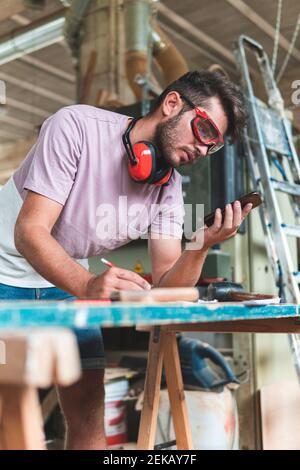Young male carpenter using smart phone while working in workshop Stock Photo