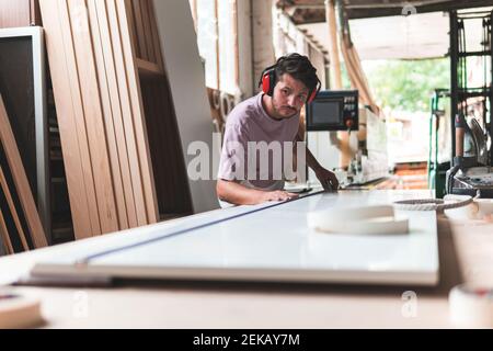 Male carpenter measuring plank using tape measure on workbench in workshop Stock Photo