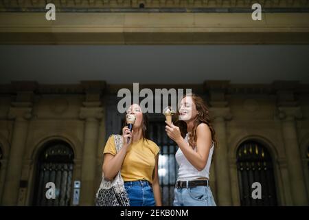 Young women eating ice cream while standing against building Stock Photo