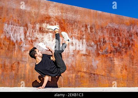 Man with face mask doing handstand against wall Stock Photo